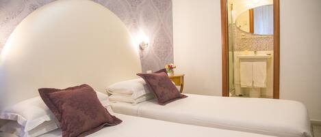 A hotel room with two beds, a large mirror, a nightstand with a lamp, and a bathroom visible through an open door.
