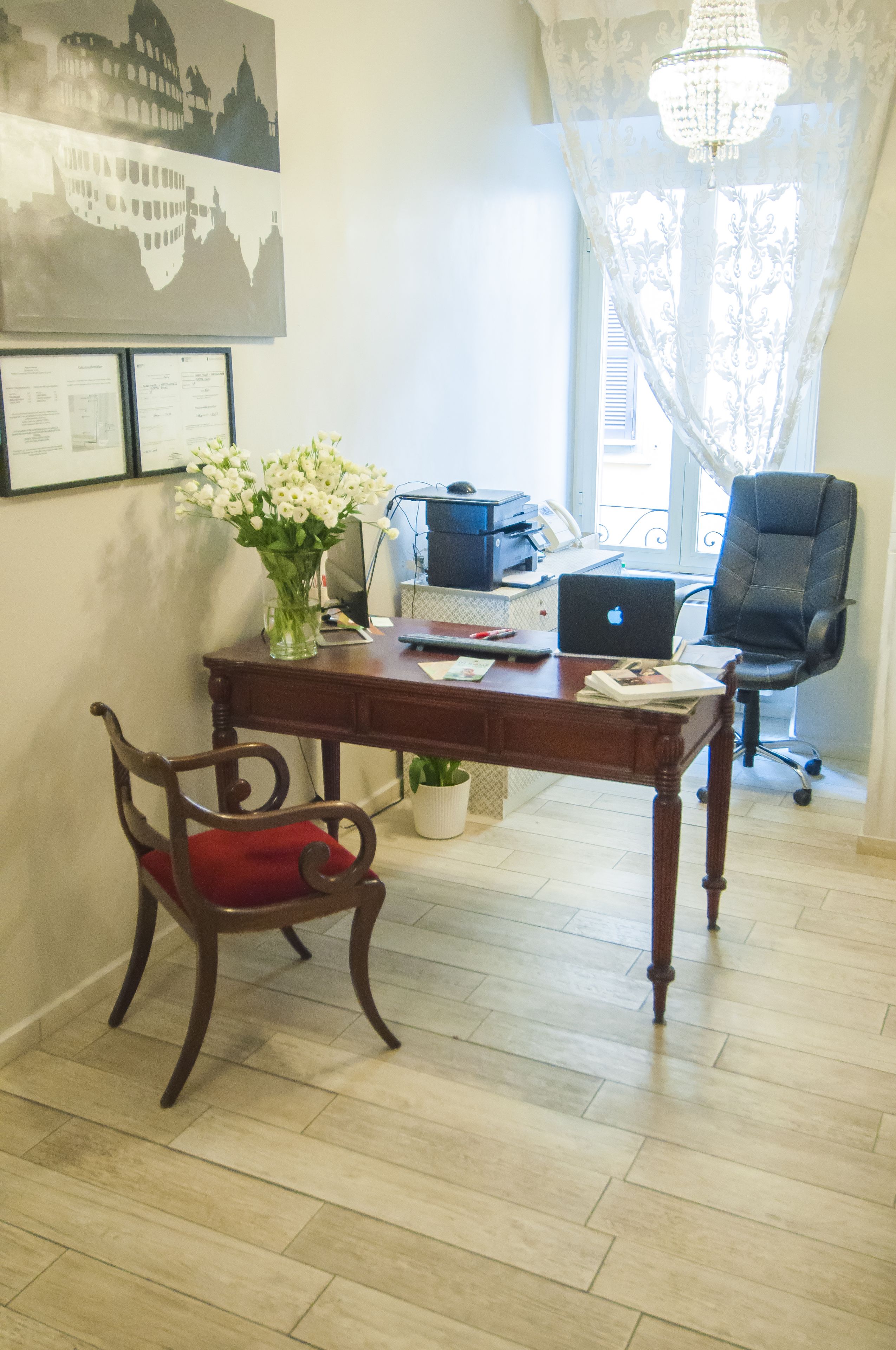 Un bureau à domicile avec un bureau en bois, un ordinateur portable, une chaise, un vase de fleurs et un lustre.