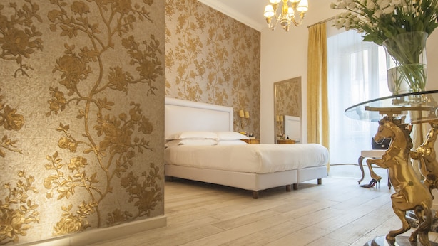 Quarto com cama, um candelabro, um vaso com flores e uma estátua dourada de cavalo.