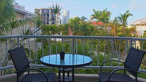 A balcony with a round table and two chairs, overlooking a cityscape with palm trees and buildings. - Surfers Del Rey (Surfers Paradise)
