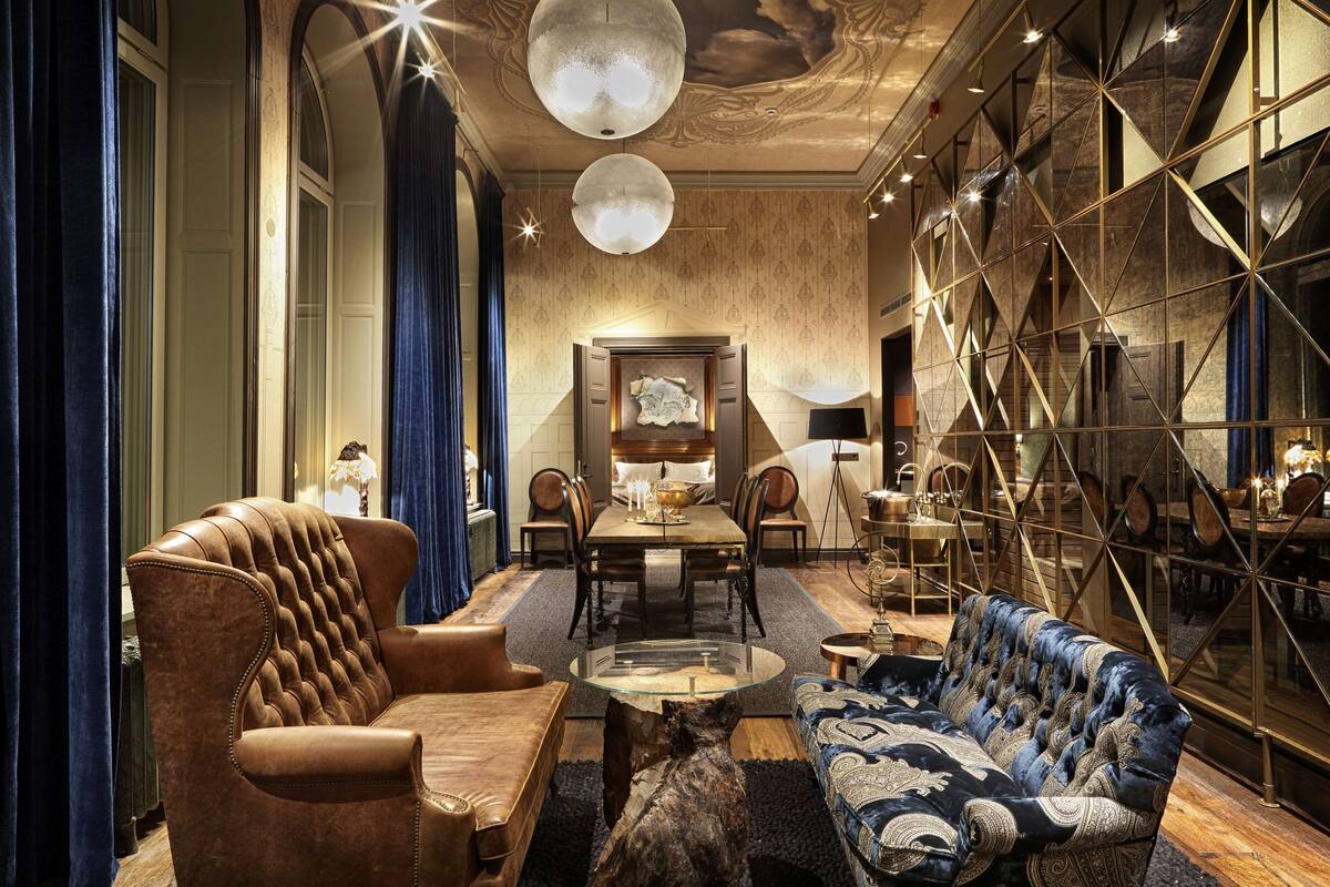 A luxurious interior with a leather armchair, a patterned sofa, a dining table, and a chandelier.