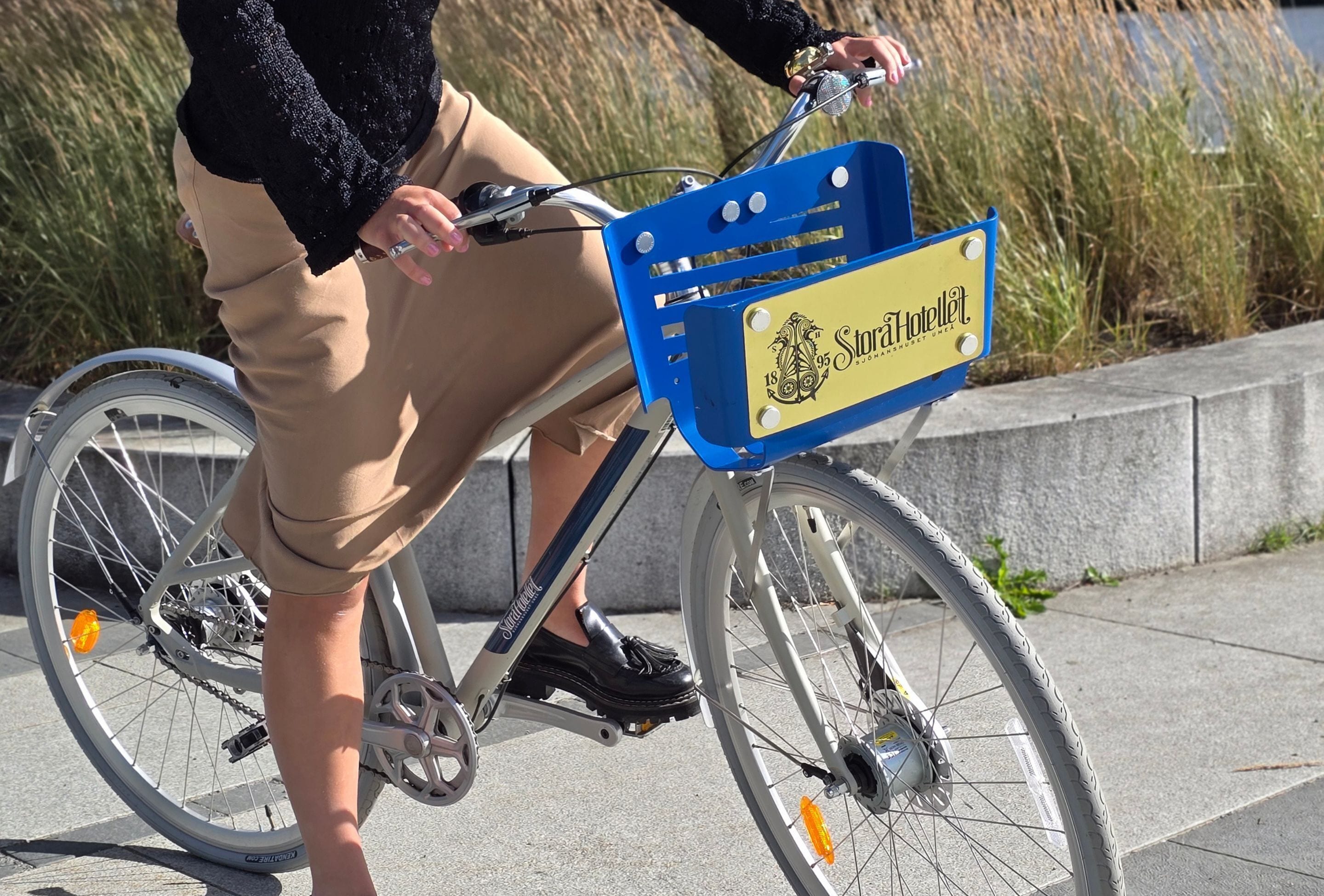 Uma bicicleta com uma caixa de armazenamento azul e amarela identificada com 'Stora Hotellet' na frente.