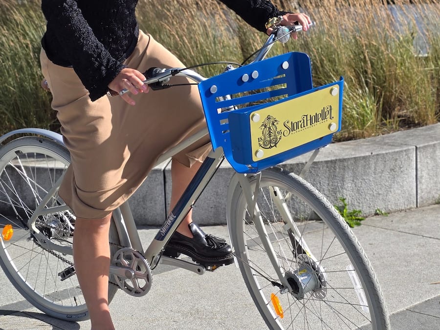 Uma bicicleta com uma caixa de armazenamento azul e amarela identificada com 'Stora Hotellet' na frente.