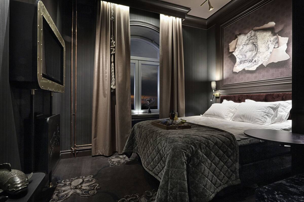 A hotel room with a large bed, a round table, a mirror, and a decorative headboard.