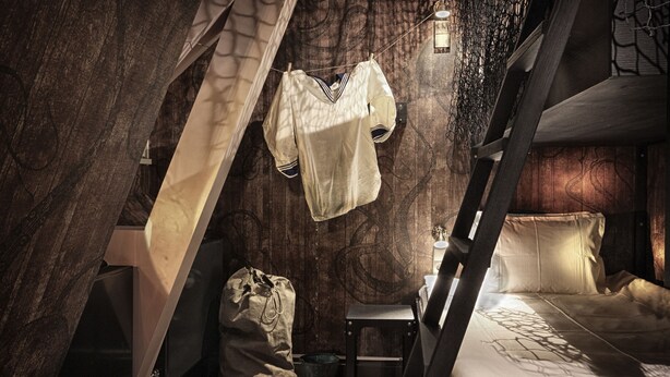 A compact, rustic room with a bed, a small table, and a hanging garment. - Stora Hotellet, BW Premier Collection (Umea)