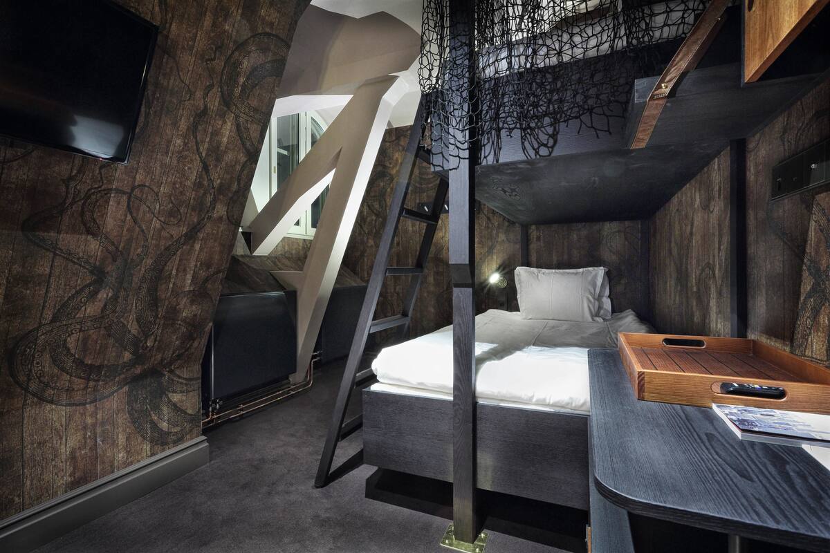 A modern room with a bunk bed, a desk with a tray, and a TV mounted on the wall.