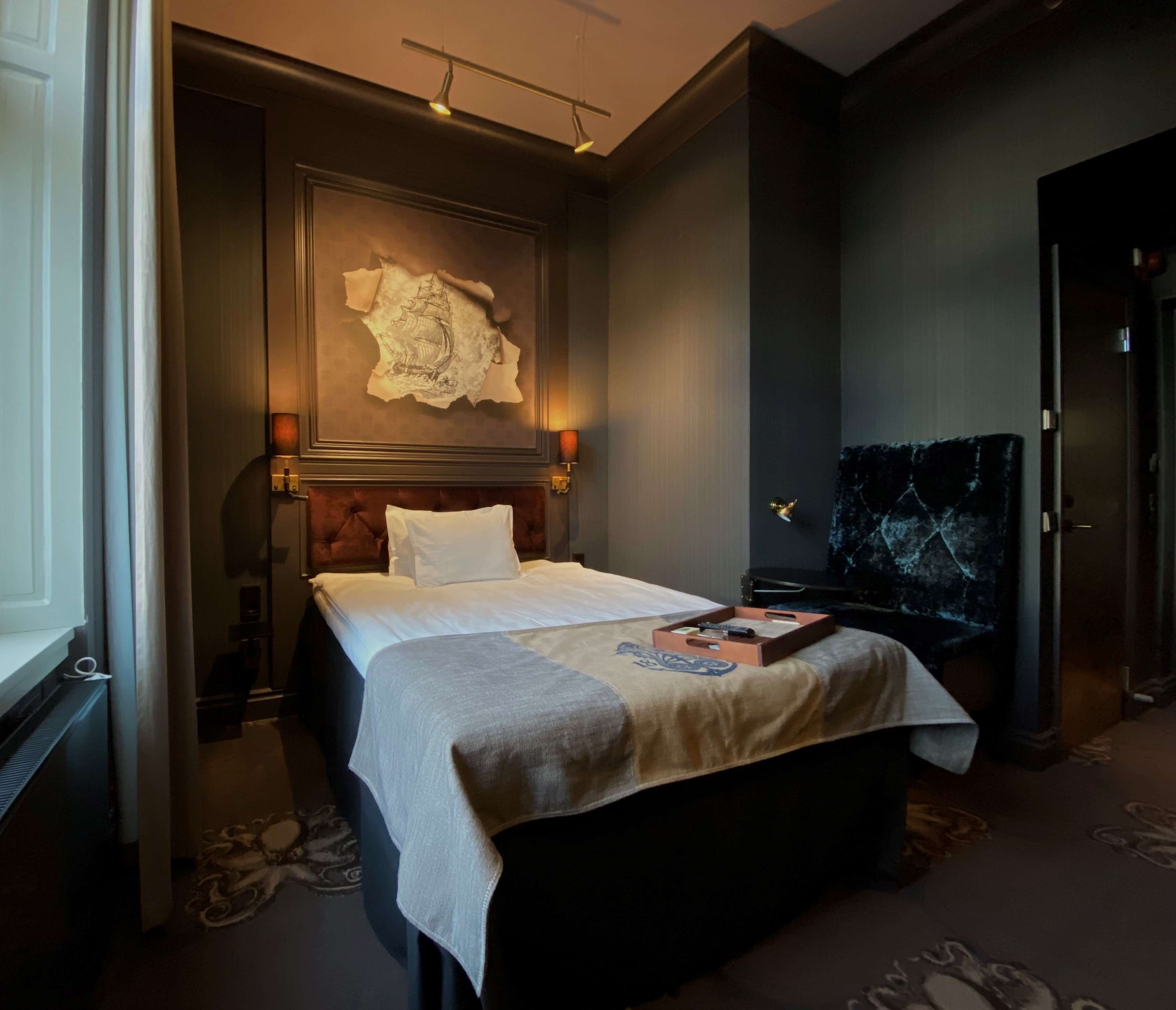 Une chambre d’hôtel avec un grand lit, un élément décoratif mural et une tête de lit de couleur sombre.
