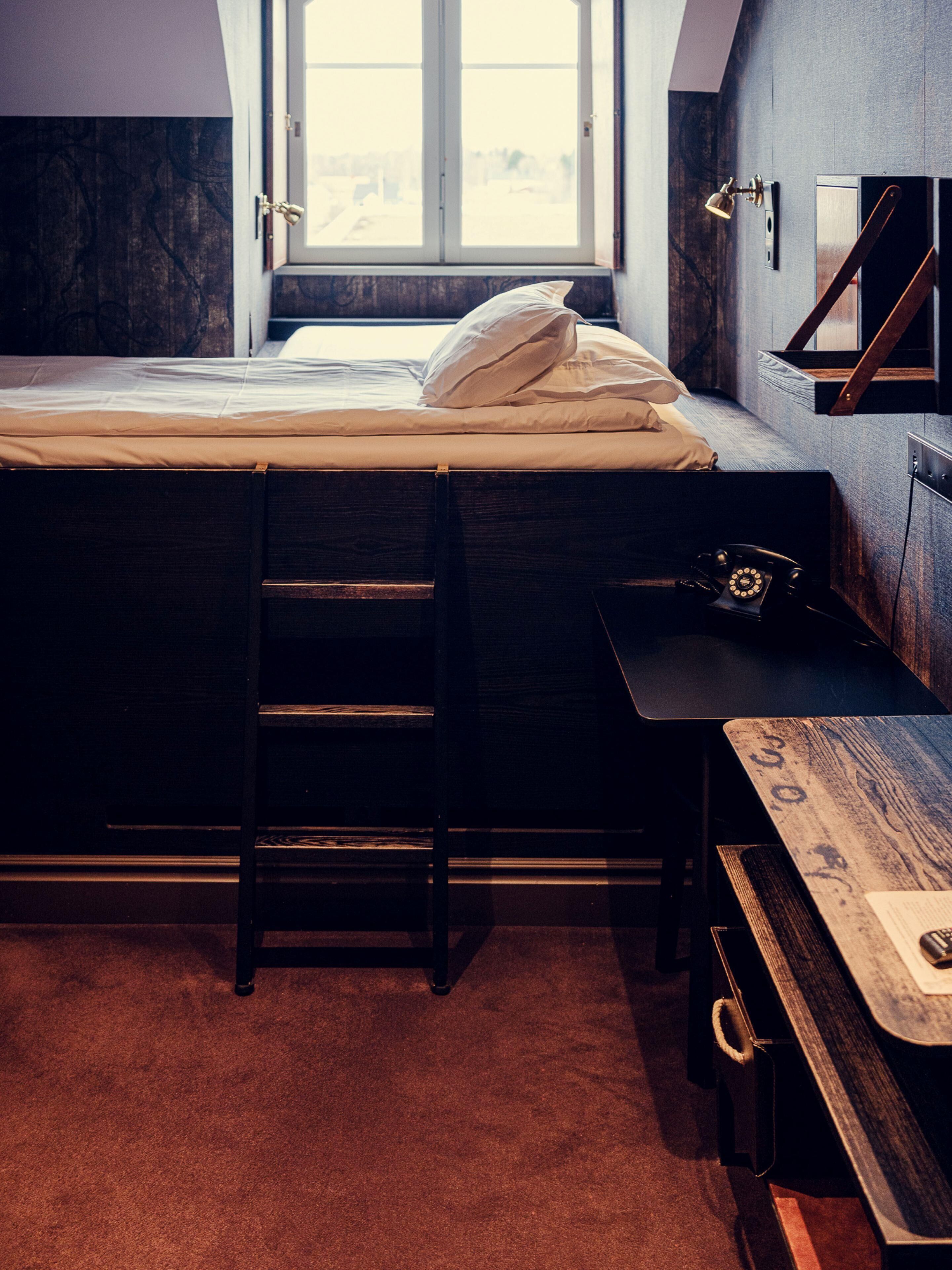 A bedroom with a bed, a desk, a ladder, and a window.