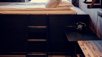 A bedroom with a bed, a desk, a ladder, and a window.