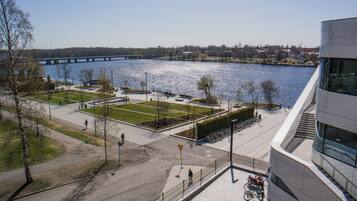 A riverside park with a bridge in the background, a modern building with large windows, and a paved walkway.