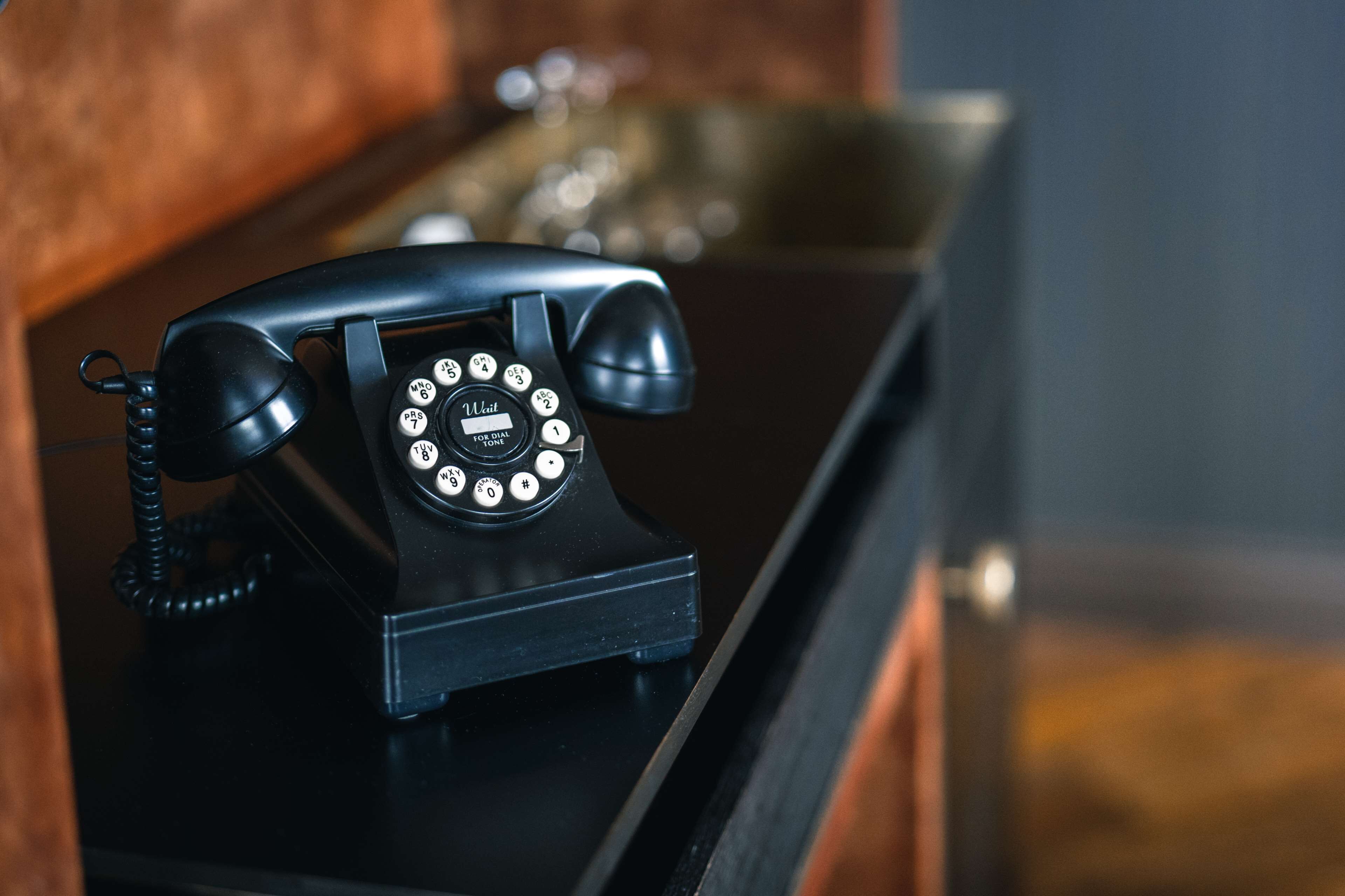 Un teléfono con dial rotatorio negro sobre un escritorio de madera.