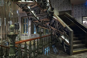 A staircase with ornate metal railings and a wooden handrail, leading to a landing with a window.