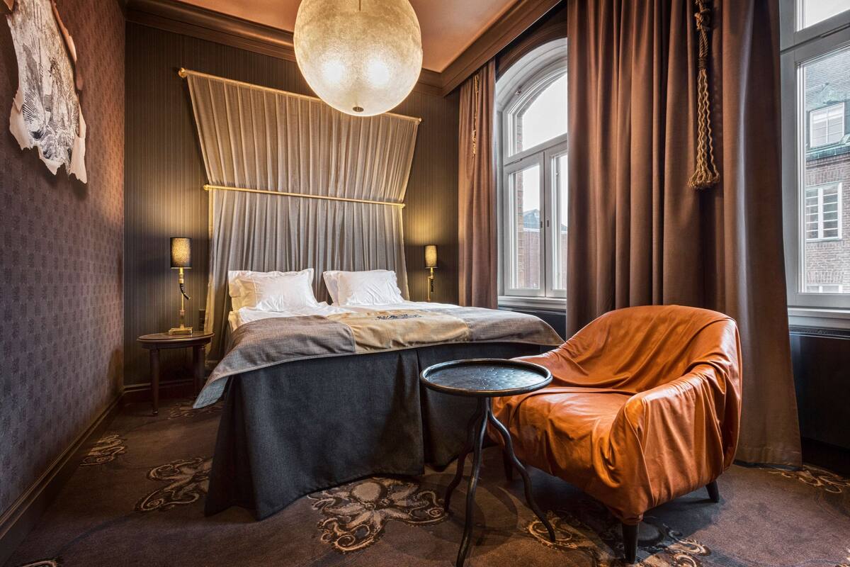 A hotel room with a bed, a chair, a small table, and a large window.