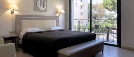 A modern hotel room with a large bed, two bedside lamps, a bench, and a balcony with outdoor furniture.
