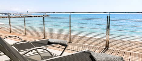 A deck with lounge chairs overlooking a beach and the sea.