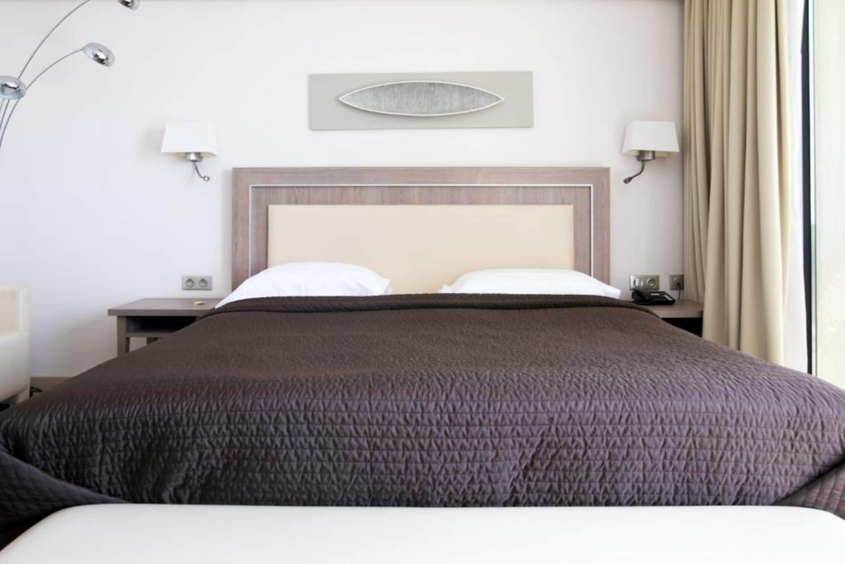 A hotel room with a large bed, two bedside tables, a modern lamp, and a wall-mounted light fixture.