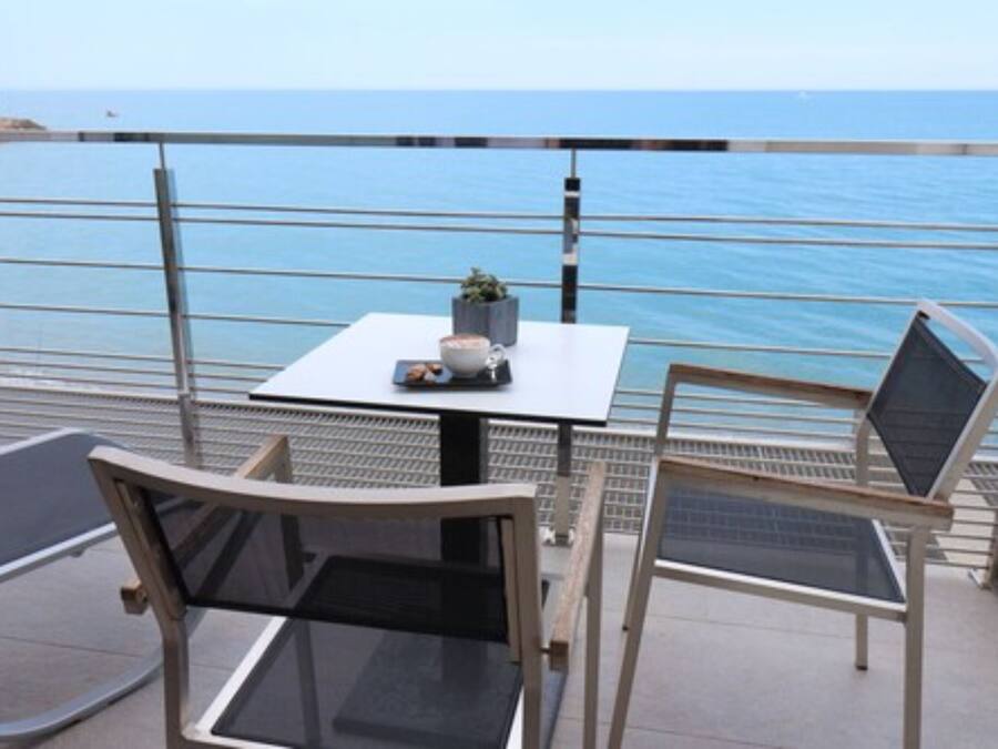 A balcony with a table and chairs, overlooking a calm sea and a lighthouse in the distance.