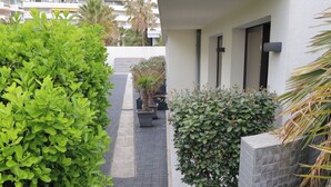 A narrow pathway flanked by lush green hedges and a modern building with a tiled exterior. - Hotel Villa Azur (Villeneuve-Loubet)