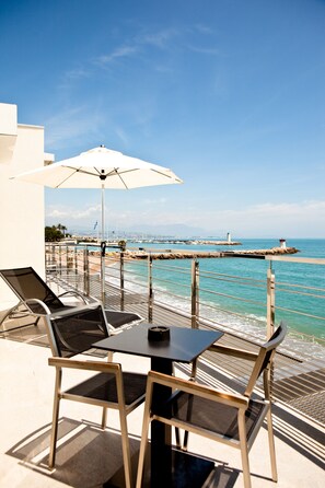 A balcony with a table and chairs, overlooking a coastal area with a pier and a lighthouse. - Hotel Villa Azur (Villeneuve-Loubet)