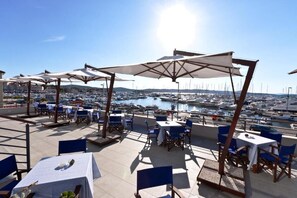 A terrace with tables and chairs, overlooking a marina with boats. - Hotel IN (Biograd na Moru)