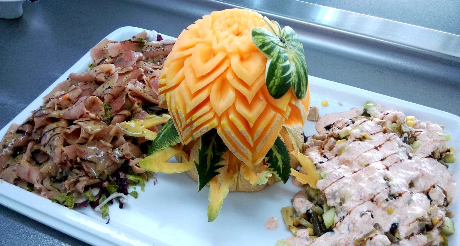 A plate with three different dishes: a salad with shredded meat, a carved melon, and a creamy chicken salad.