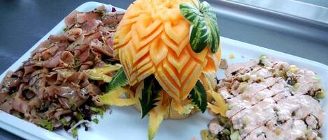 A plate with three different dishes: a salad with shredded meat, a carved melon, and a creamy chicken salad.