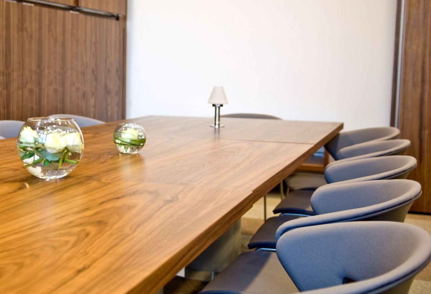 Ein Konferenzraum mit einem Holztisch, zwei Glasvasen mit Blumen und einer Lampe.