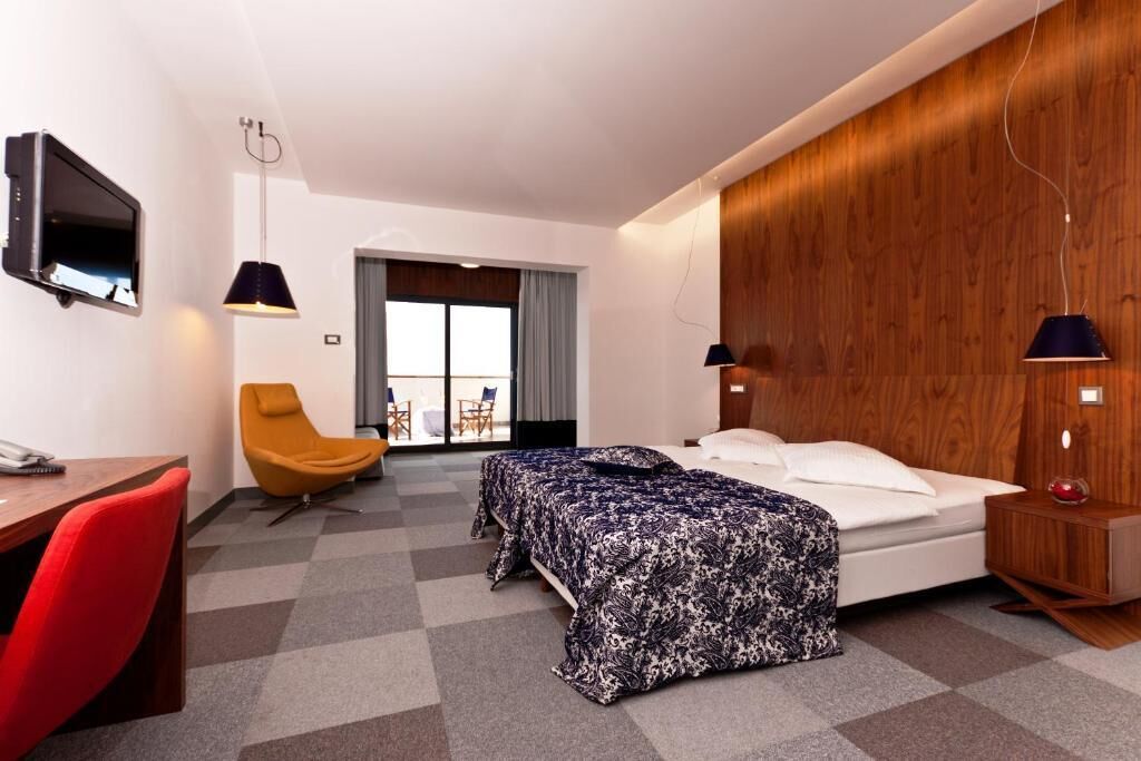 Quarto de hotel com cama, escrivaninha, cadeira e televisão.