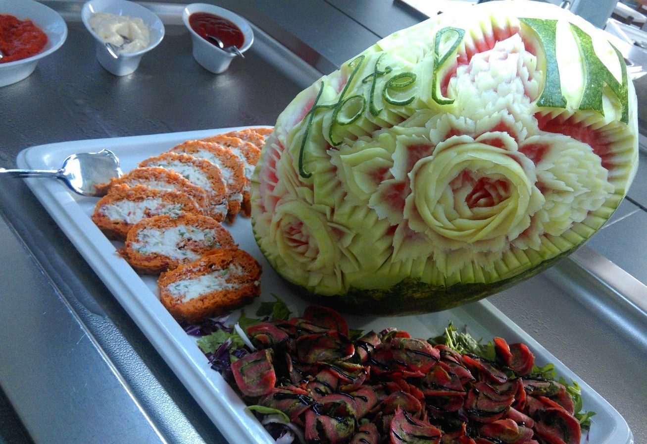 En utskuren vattenmelon med ett blommönster, en tallrik med panerade kotletter och en sallad.