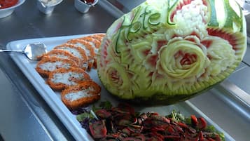 En utskuren vattenmelon med ett blommönster, en tallrik med panerade kotletter och en sallad.