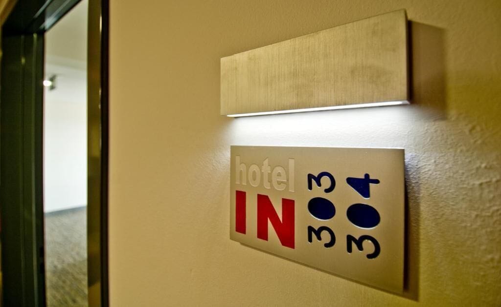 Un letrero de habitación de hotel con el texto 'hotel IN 303 304' en una pared color crema.