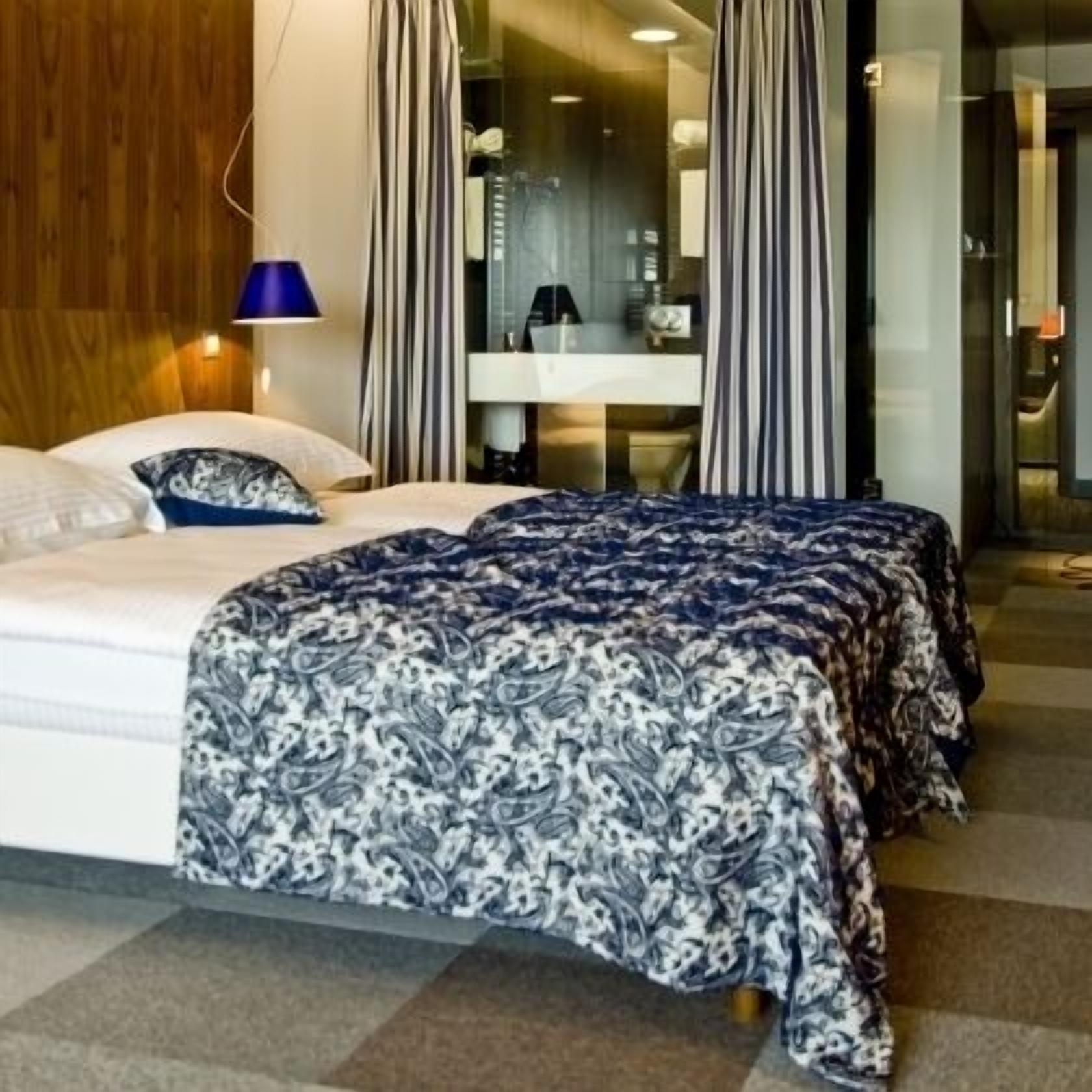 Camera d'albergo con un letto, un comodino, una lampada e un bagno visibile attraverso una porta di vetro.