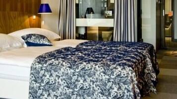 A hotel room with a bed, a nightstand, a lamp, and a bathroom visible through a glass door.