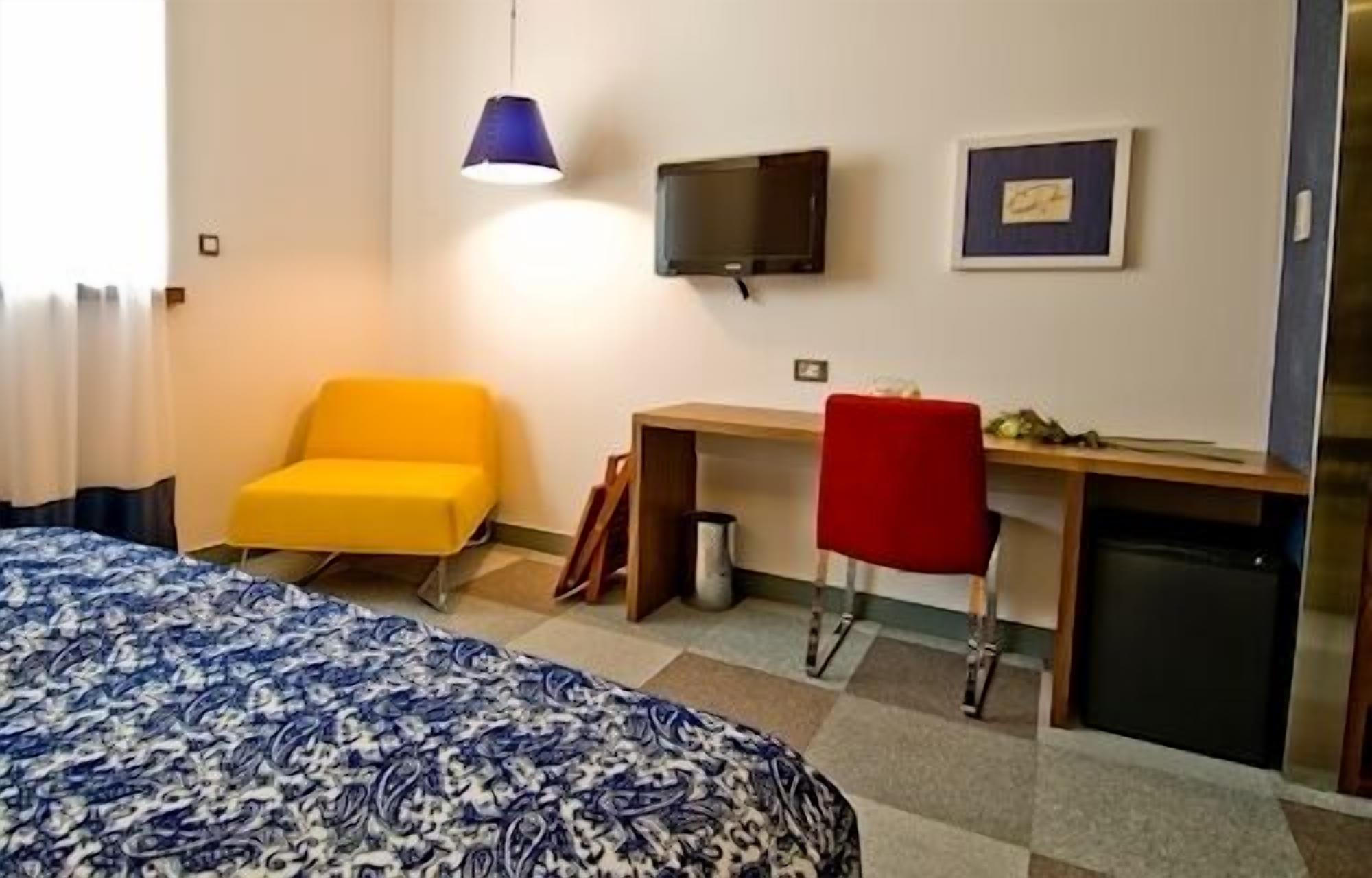 Una habitación de hotel con cama, escritorio, silla, televisor y un refrigerador pequeño.