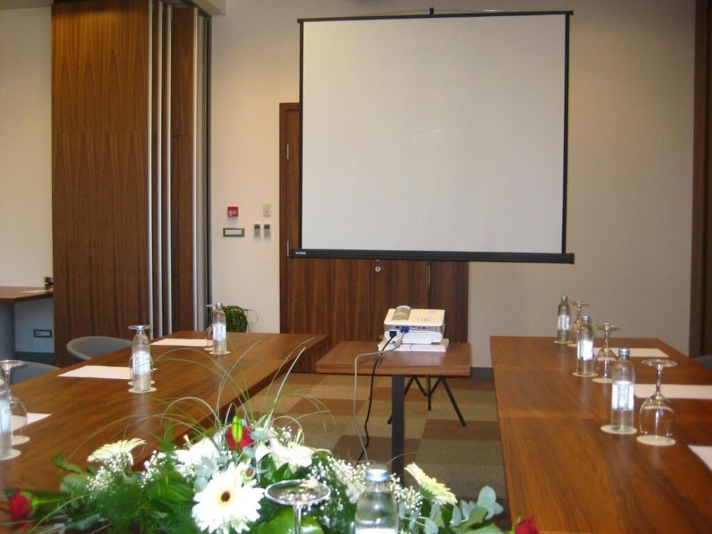 Ett konferensrum med en stor skärm, bord i trä och blomsterarrangemang som mittpunkter.