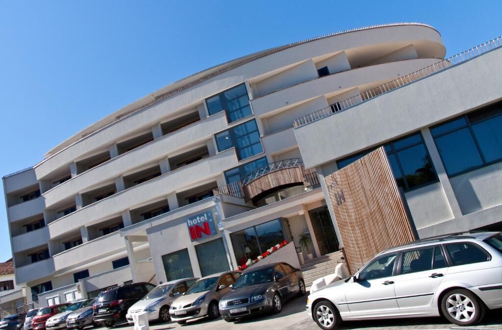 Un hôtel à plusieurs étages, doté d’un design moderne, avec des balcons aux étages supérieurs et un parking pouvant accueillir plusieurs voitures.
