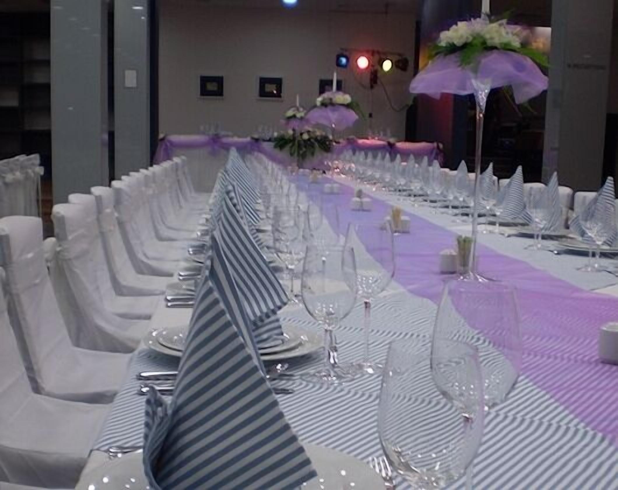 A long banquet table with white chairs and purple tablecloths, set for a formal event.