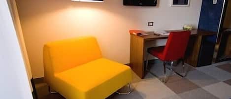 A room with a yellow chair, a desk with a red chair, a television, and a blue lamp.