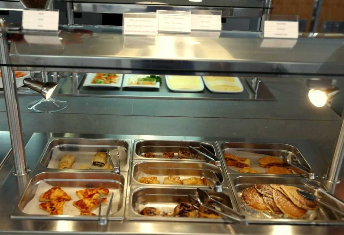 A buffet with various food items in trays, including pizza, pastries, and other dishes.