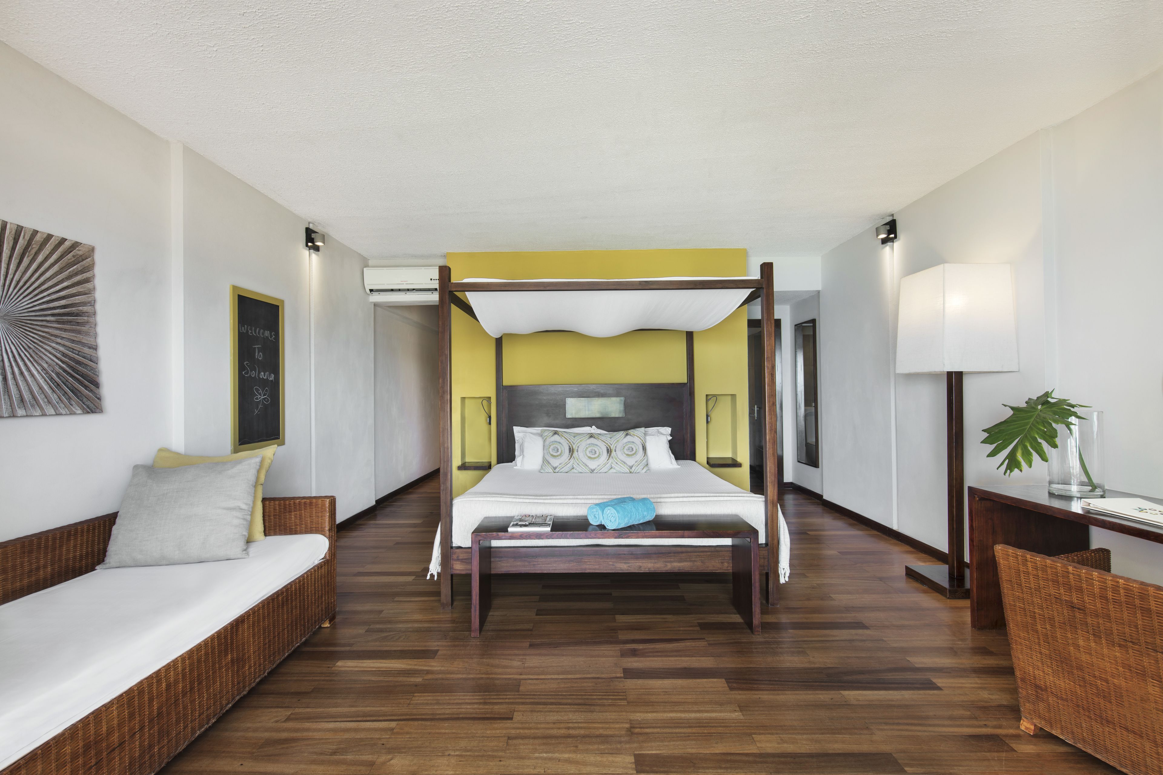 A spacious room with a large bed, a sofa, and a bedside table with a lamp.