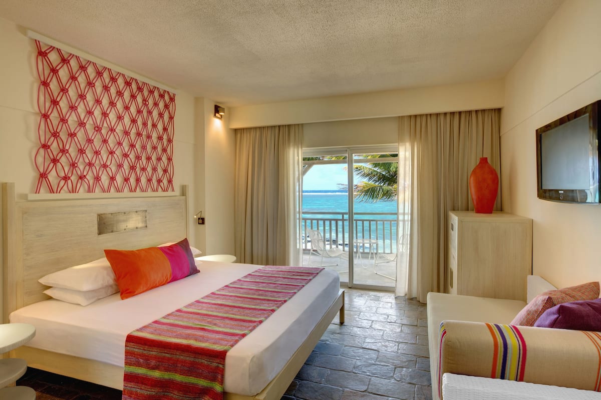 Une chambre d’hôtel comprenant un lit, une télévision, un balcon avec vue sur la mer et un élément décoratif mural.