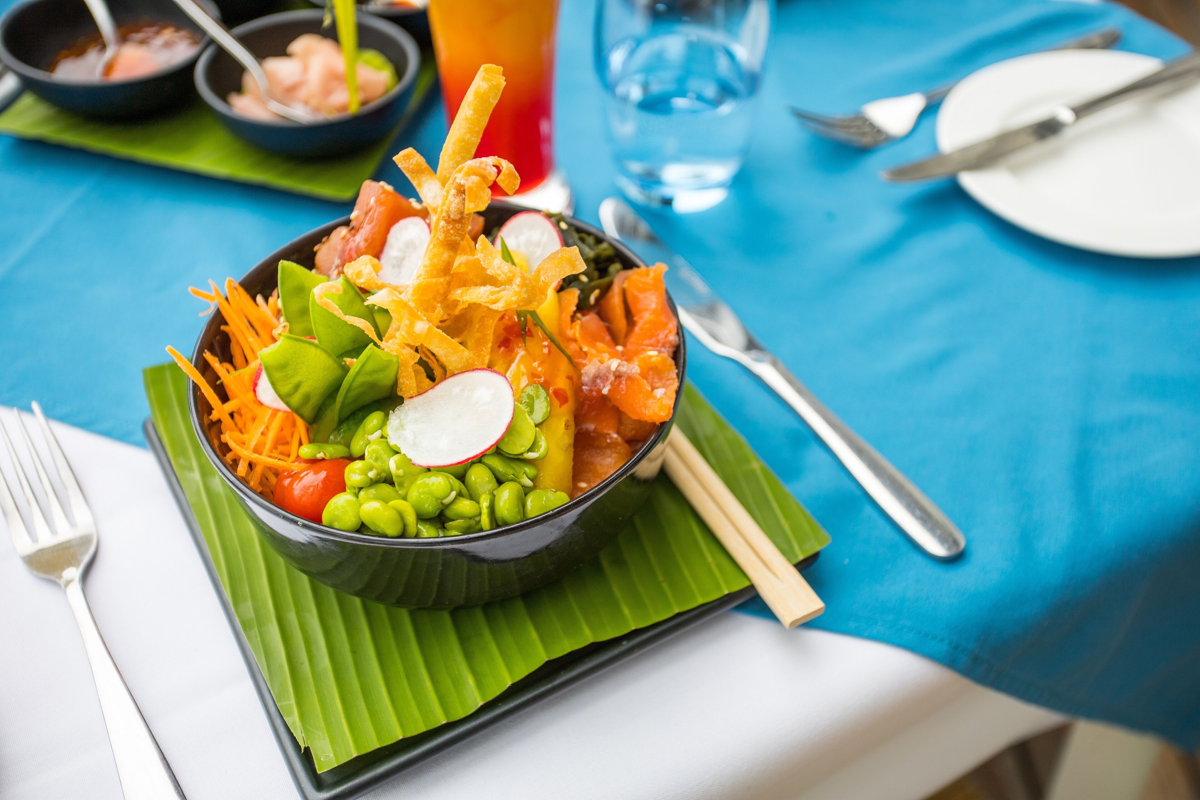 A meal with various vegetables and fish on a green leaf, served on a black bowl.