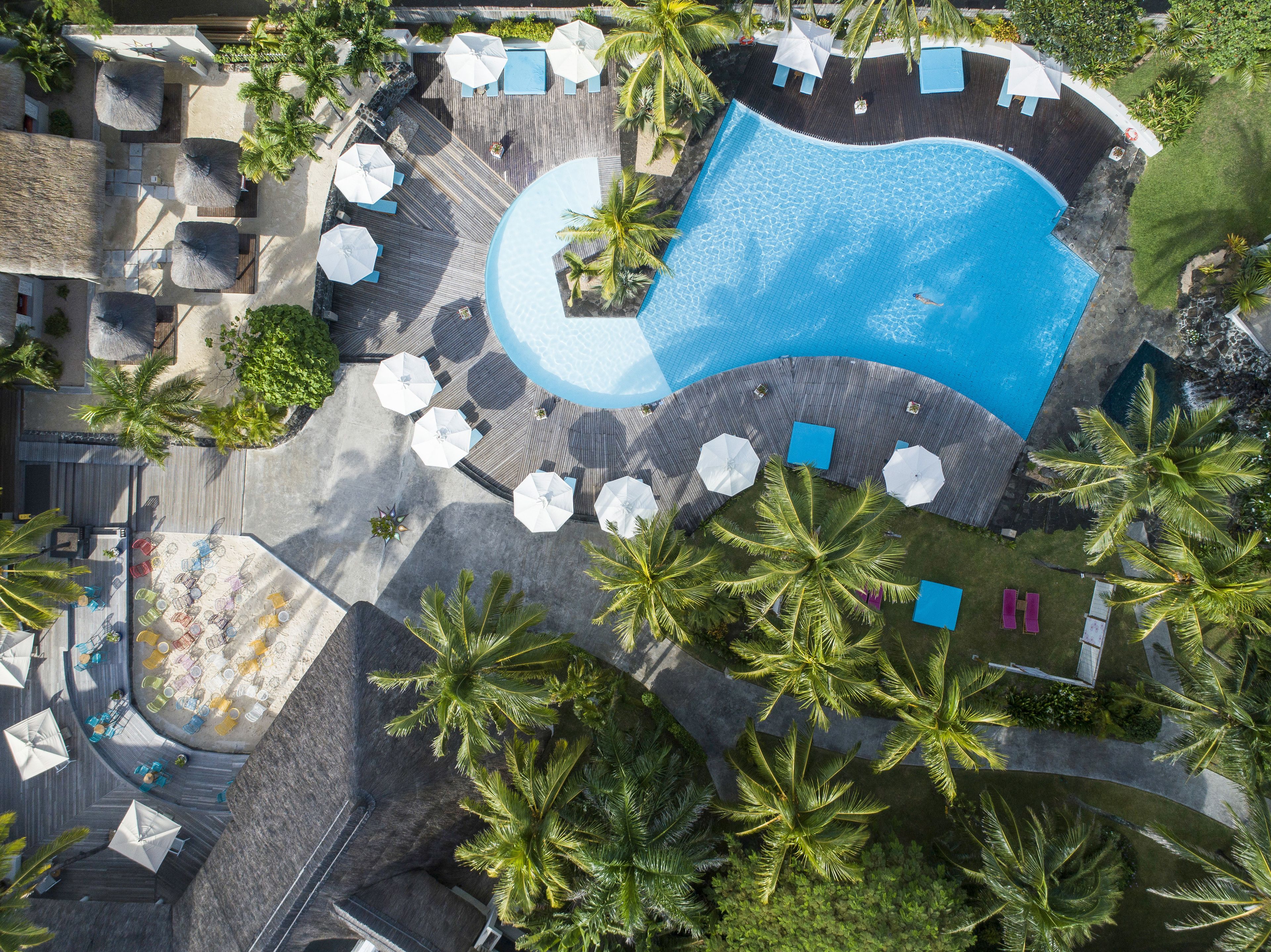 Vista aérea de un complejo turístico con una gran piscina, tumbonas y palmeras.