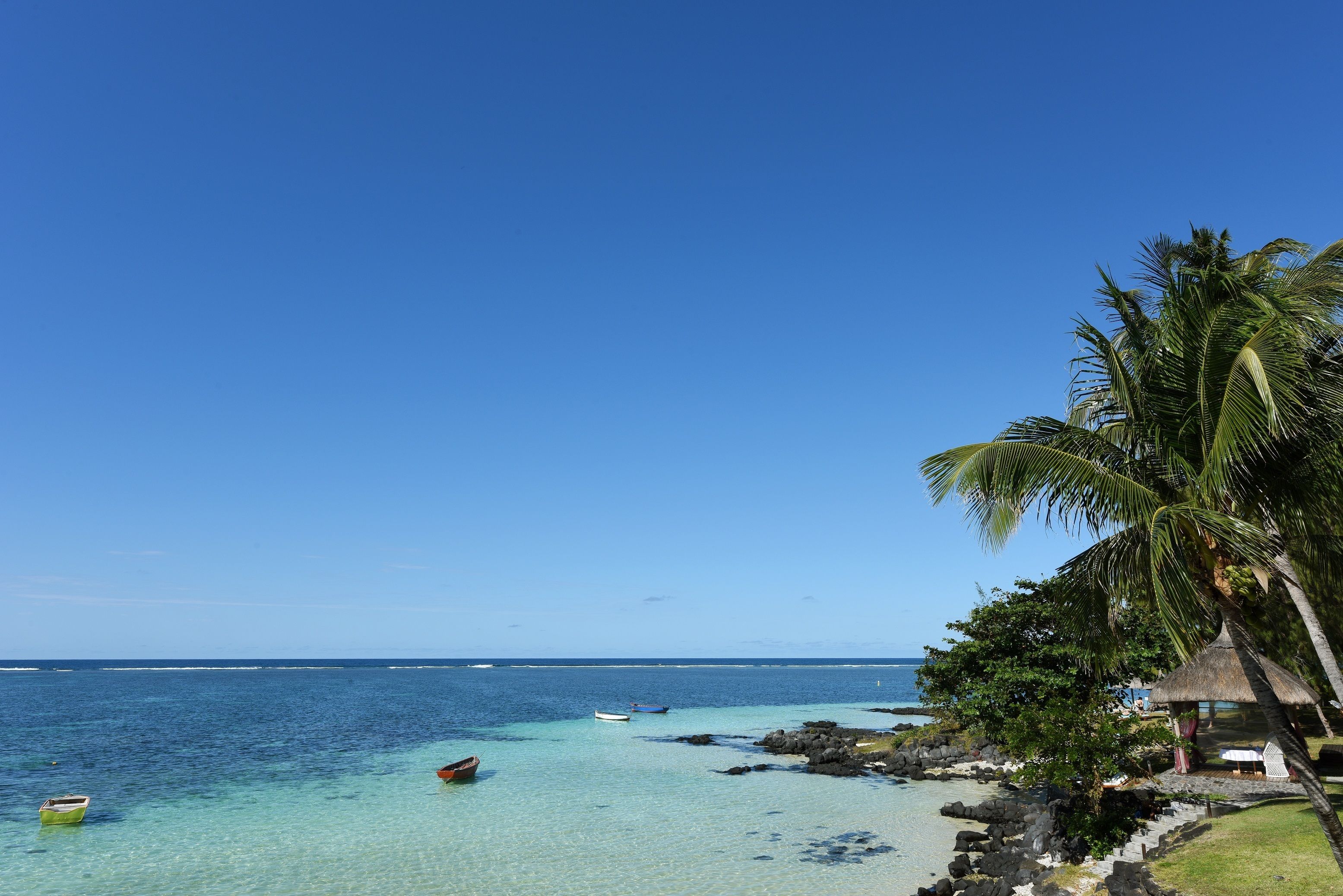 Une plage à l’eau turquoise et limpide, une cabane au toit de chaume et des palmiers.