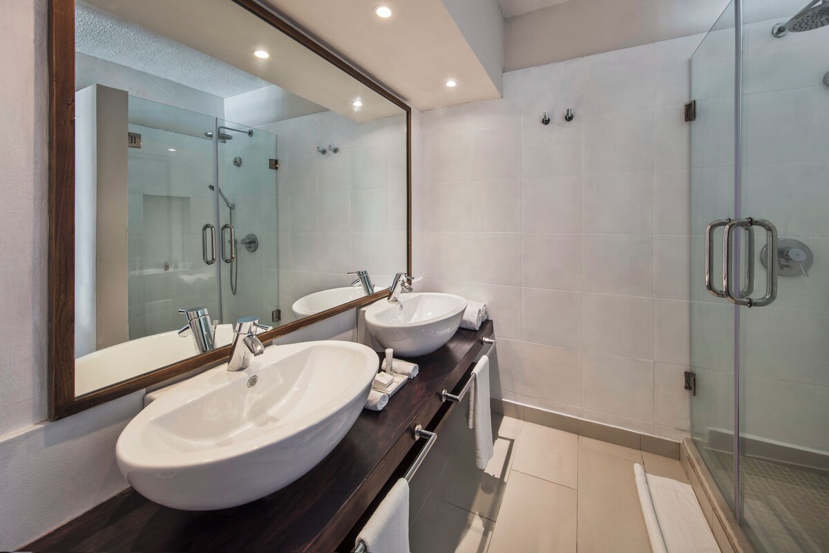 A modern bathroom with two sinks, a large mirror, and a glass shower enclosure.