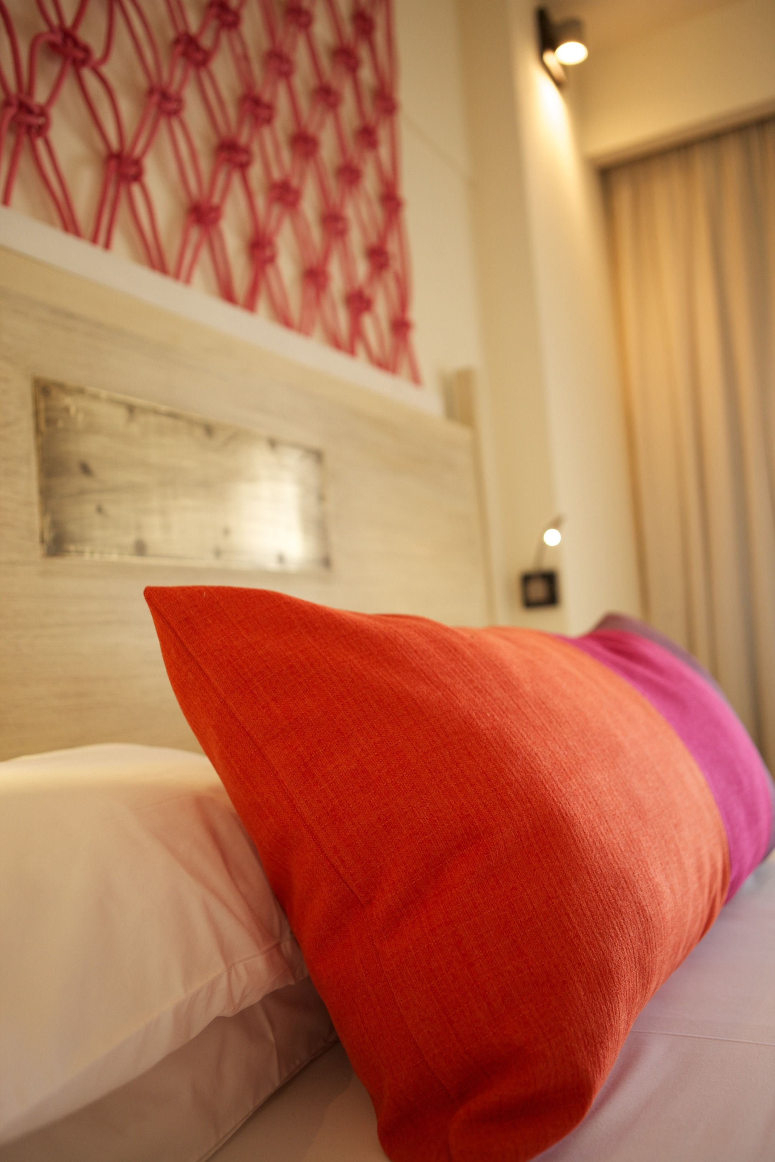 Una cama con un cojín blanco y rosa, un cojín rojo y un cabecero de madera.