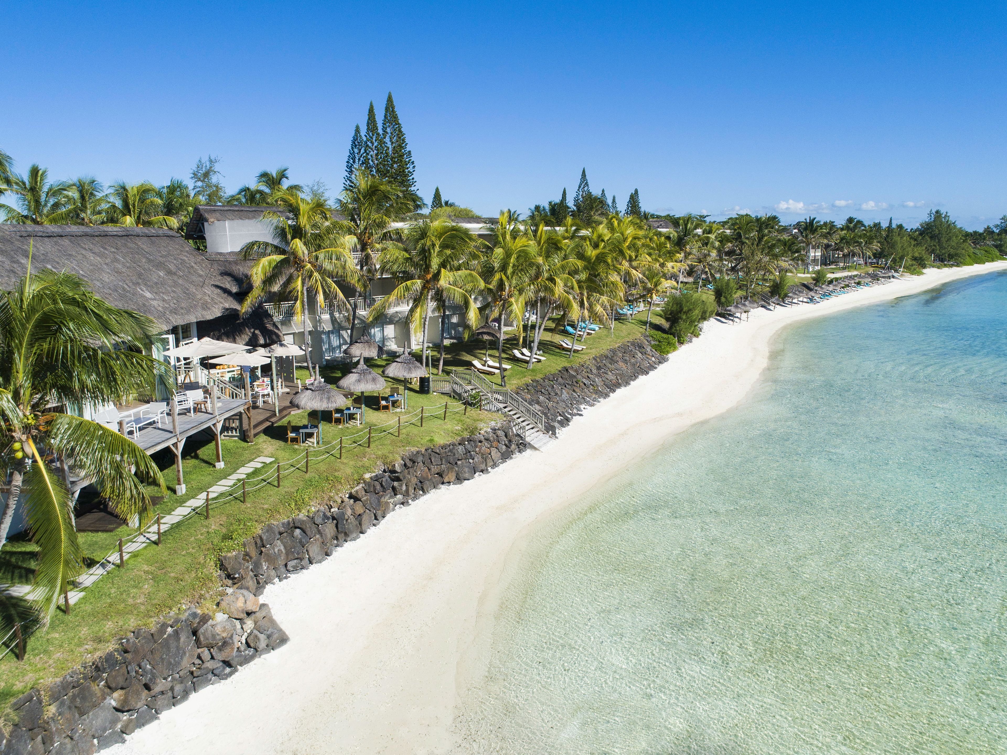 A beach resort with a thatched-roof building, palm trees, and a clear blue sea.