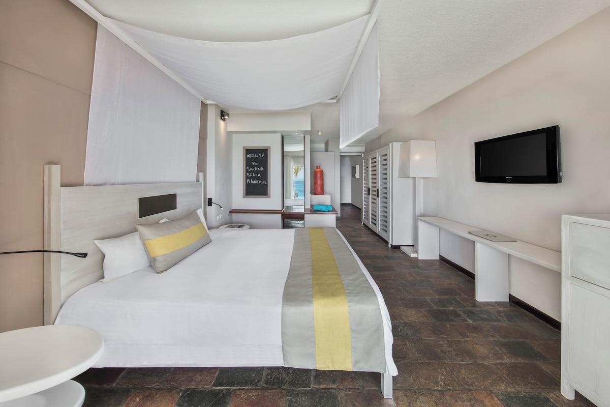Habitación de hotel con una cama grande, un escritorio, una silla, un televisor y un baño visible a través de una puerta abierta.