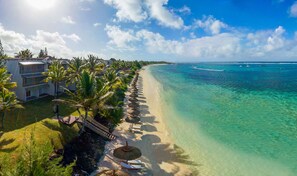A beachfront hotel with a palm tree-lined walkway, clear turquoise waters, and a view of the ocean. - Solana Beach - Adults Only (Belle Mare)