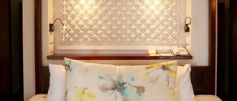 Una habitación de hotel con cama, un panel decorativo, teléfono y una pequeña estantería.